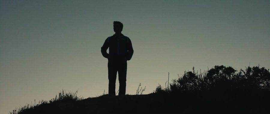 A man stands silhouetted on a hilltop at dusk
