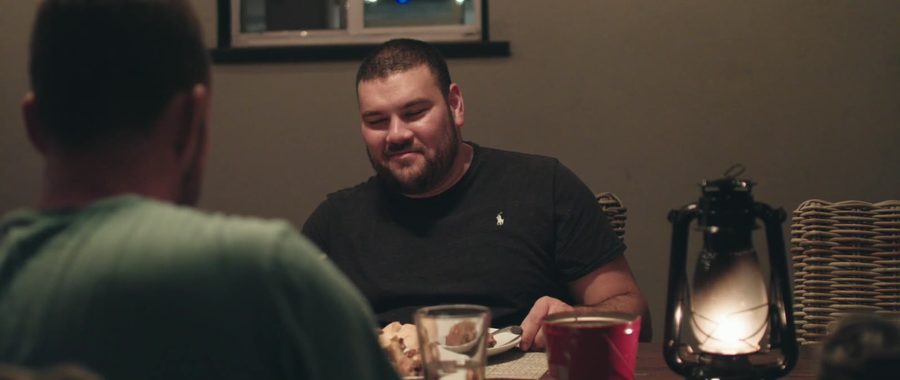 Two men talk over dinner by lantern light