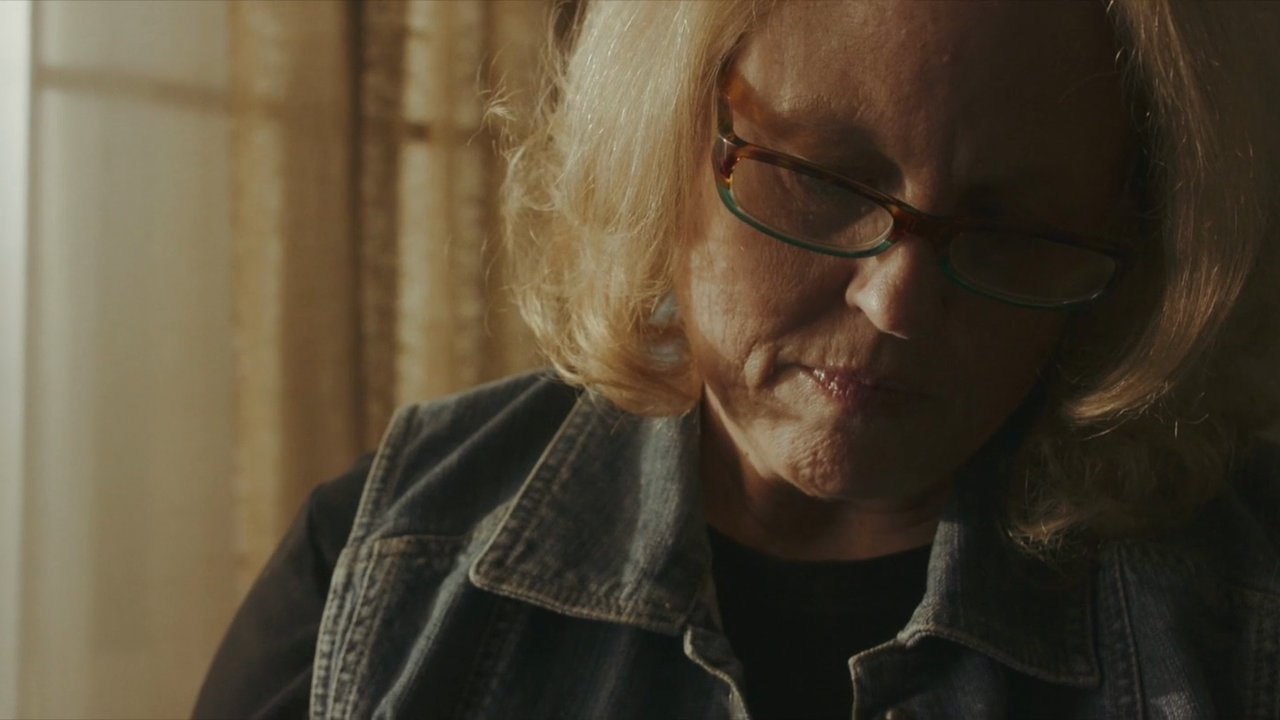 A woman in glasses looks down, lit by a window